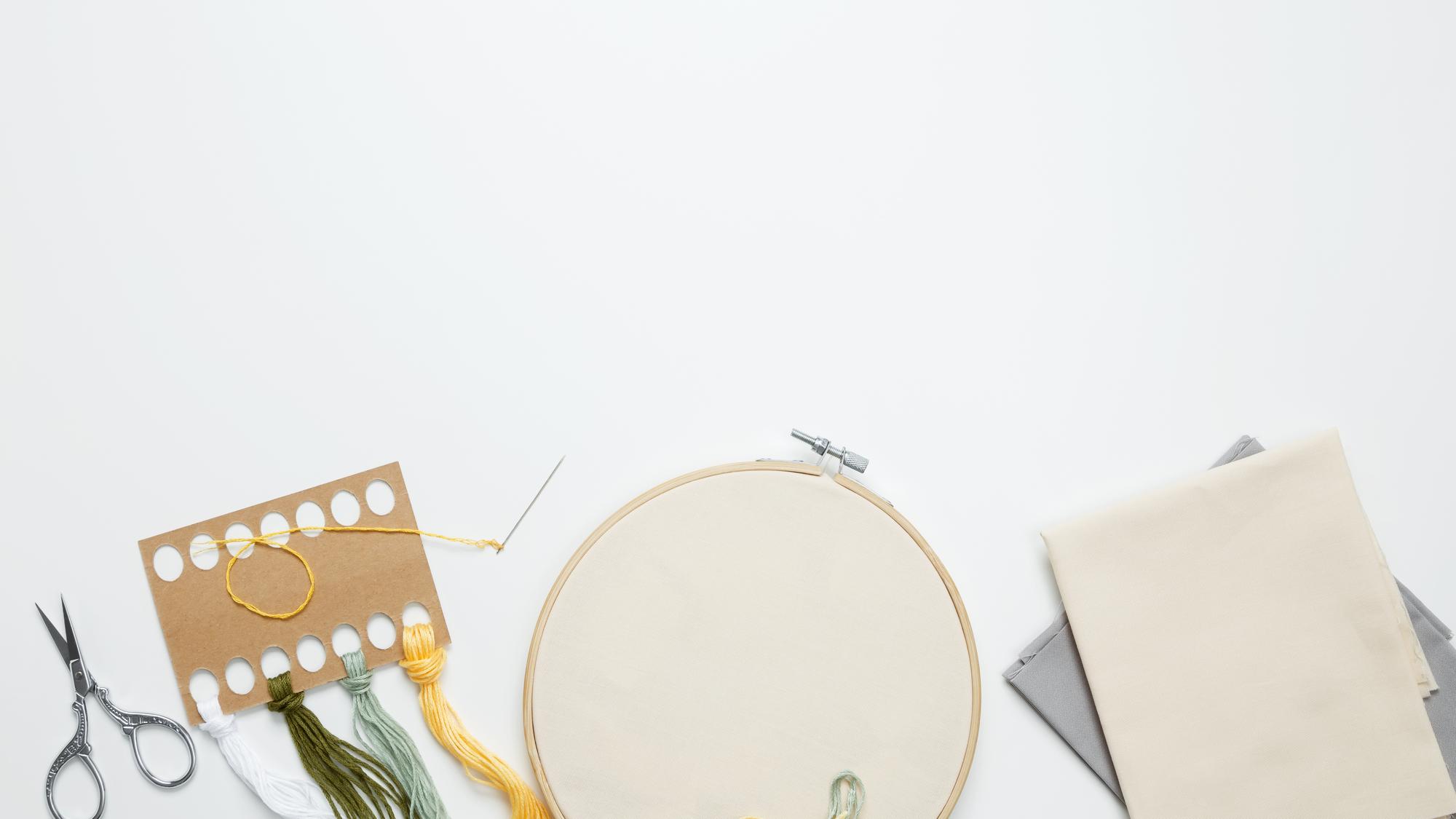 atelier table with threads, hoops and a finished embroidered sampler